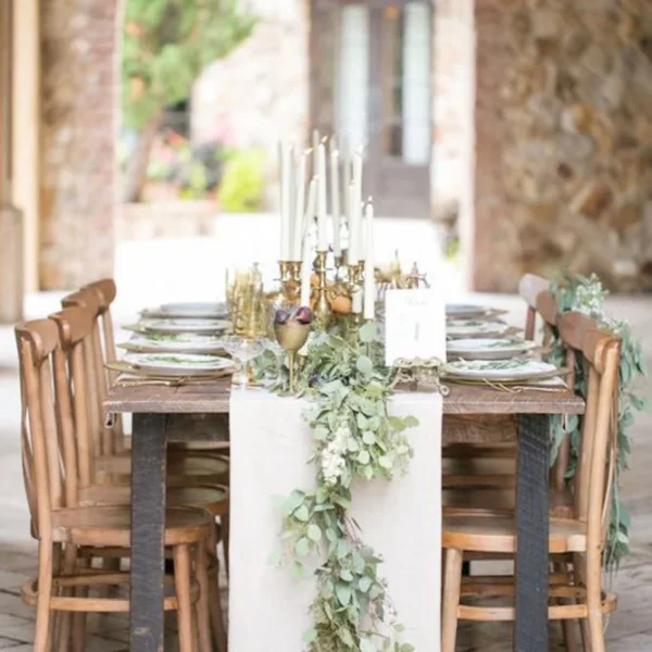 Long rustic table with a greenery runner and candles beneath a stone archway at Deux Belettes