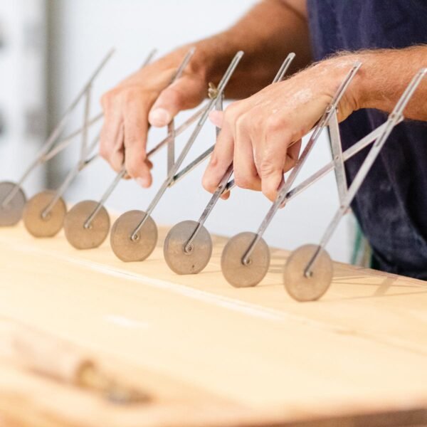 Hands rolling a multi-blade pasta cutter across fresh pasta dough